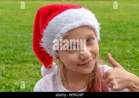 Affascinante 8 anni ragazza di santa claus hat solleva un dito verso l'alto e sorrisi. Natale. Anno nuovo concetto di spazio di copia Foto Stock