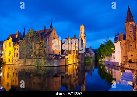 Il campanile e gli edifici illuminati di notte lungo un canale nel centro storico di Bruges, sito Patrimonio Mondiale dell'UNESCO, Belgio, Europa Foto Stock