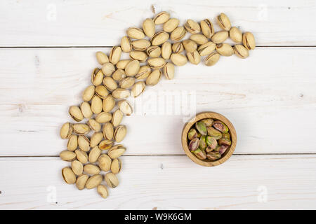 Sacco di tutto mature pistacchio verde nella piccola ciotola di legno flatlay su legno bianco Foto Stock