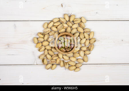 Sacco di tutto mature pistacchio verde nella piccola ciotola di legno flatlay su legno bianco Foto Stock