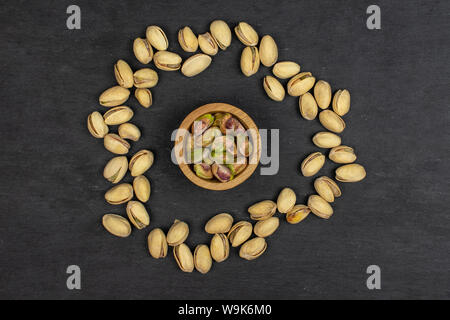 Sacco di tutto mature pistacchio verde nella piccola ciotola di legno flatlay sulla pietra grigia Foto Stock