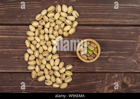 Sacco di tutto mature pistacchio verde nella piccola ciotola di legno flatlay su legno marrone Foto Stock