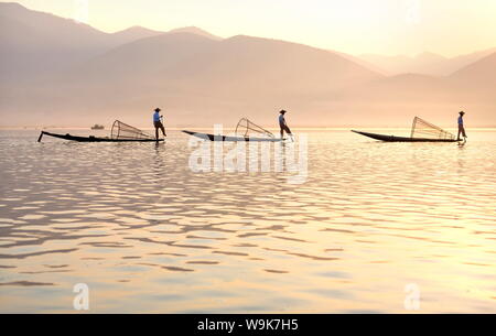 Intha "gamba" a remi dei pescatori al tramonto sul Lago Inle che pescano con reti tesa su conica telai di bambù, Lago Inle, Myanmar Foto Stock