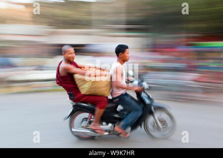 Panoramiche e sfocata shot la creazione di un senso di movimento, monaco buddista riding pillion e portante le verdure sul retro di un ciclomotore, Mandalay Myanmar Foto Stock