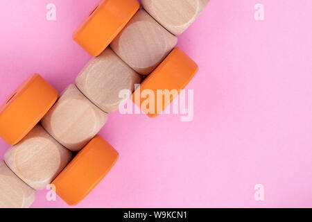 Vista dall'alto sui bambini gioco educativo sulla luce rosa di sfondo della carta. Treno in legno realizzato dai cubi, cerchi di colore arancione. Close up. Foto Stock