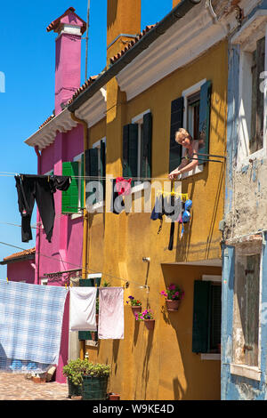 Signora pende lavaggio fuori dalla sua finestra cottage, Mandracchio, Burano, Laguna Veneziana, Veneto, Italia Foto Stock