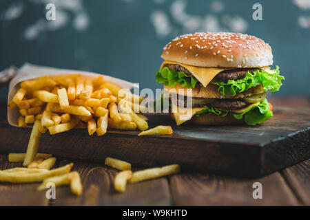 Burger con patate e birra scura su una tavola di legno su un blu-grigio Foto Stock