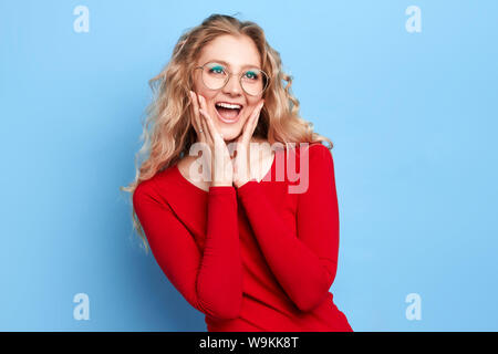 Crazy vendita, sconti Ritratto di elegante allegro positivo ragazza con fiera lunghi capelli ondulati in abiti casual , aperto bocca, palme le guance di contenimento,looki Foto Stock