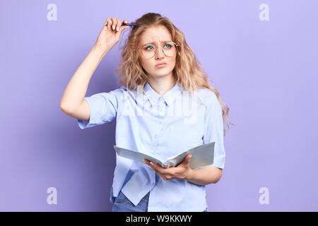 Ragazza pensice graffiare la sua testa con penna e guardando in alto, cercando di rispondere alla domanda, close up ritratto, espressione facciale Foto Stock