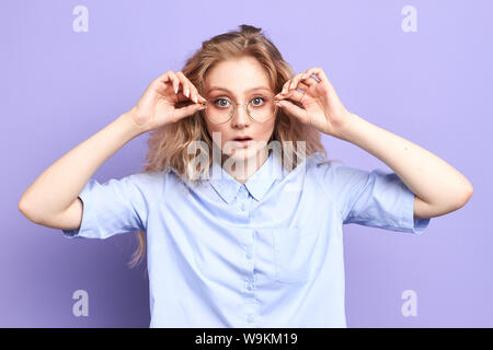 Wow non credo Close up ritratto di stupito la ragazza con la bocca aperta e gli occhi bugged, toccando i suoi occhiali isolati a sfondo blu Foto Stock