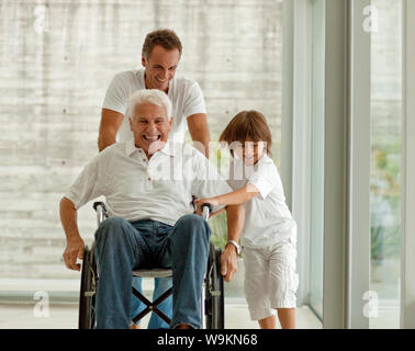 Senior uomo essendo spinto in sedia a rotelle e da suo figlio adulto e sua nipote. Foto Stock