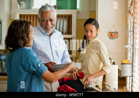 Sorridente uomo senior facendo i piatti con sua figlia adulta e nipote. Foto Stock