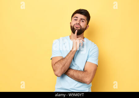 Considerato grave giovani caucasici uomo tocca mento con il dito pensando o considerando, guy rendendo la decisione o immaginando.close up verticale isolato Foto Stock
