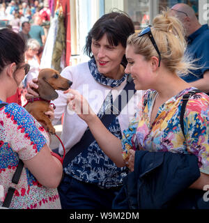 Due femmine guardando cane salsiccia portati dalla terza femmina in strada trafficata Foto Stock