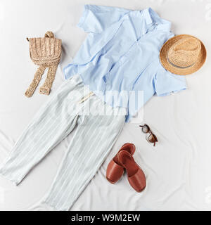 Luce maglietta blu, pantalone a righe, sandali, sacco a maglia, cappello di paglia su sfondo bianco, lifestyle, collezione di abbigliamento estivo Foto Stock