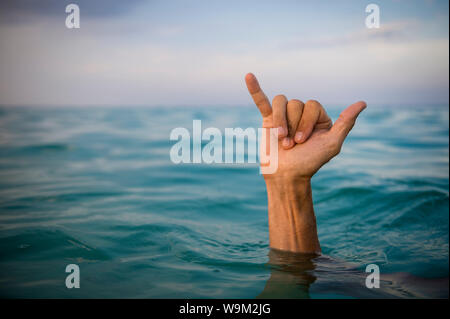 La mano del surfer rendendo shaka (appendere sciolto) Accedi le acque blu tropicali Foto Stock