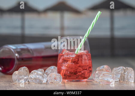 Fresca acqua rossa in vetro, acqua rosso succo di frutta, nettare rosso disseta la sete, l'acqua è una miscela di rosso e zucchero, con una bottiglia sul fondo e molti ice c Foto Stock