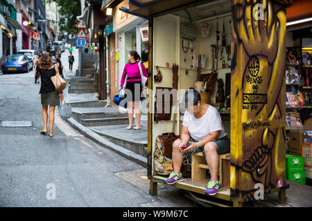 Donna ascolta musica sul suo piccolo negozio di artigianato in Hong Kong Foto Stock