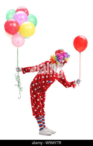 Lunghezza piena ripresa di profilo di un clown dando un pallone da un grappolo di palloncini isolati su sfondo bianco Foto Stock