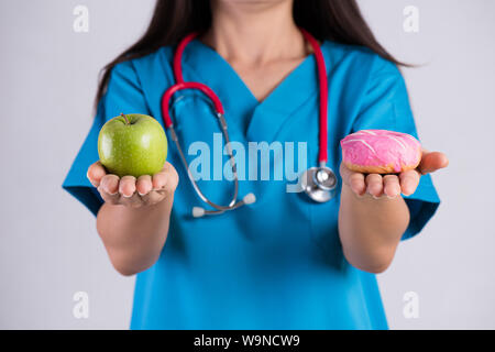 Uno stile di vita sano, cibo e sport concept. Una sana versus malsano. Medico donna mano azienda ciambella e mela verde. Foto Stock