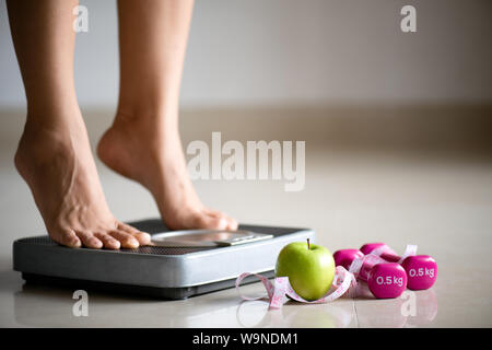 Gamba femmina intensificazione su bilance con nastro di misurazione, rosa dumbbell e mela verde. Uno stile di vita sano, cibo e sport concept. Foto Stock