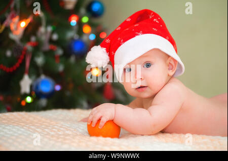 Neonato sdraiato su albero di Natale con sfondo arancione. Sdraiato sul suo ventre con un colore arancione. Vacanze di Natale. Bambino costume. Santa boy. Natale tr Foto Stock