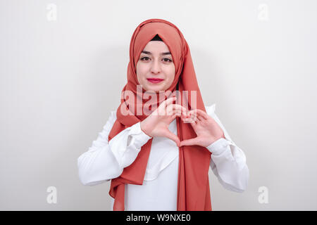 Il hijab come giovane donna musulmana facendo un gesto di cuore con le dita, ragazzina musulmana gesto di amore segno di cuore Foto Stock