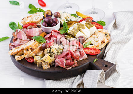Antipasto piatto con prosciutto cotto, prosciutto, salame, formaggio blu, mozzarella con pesto e olive su uno sfondo di legno. Foto Stock