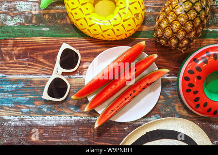 Piatto Topview lay out di anguria a fette sul piatto bianco decorato con ananas e sunglass su legno tabella ,vacanza estate concetto. Foto Stock