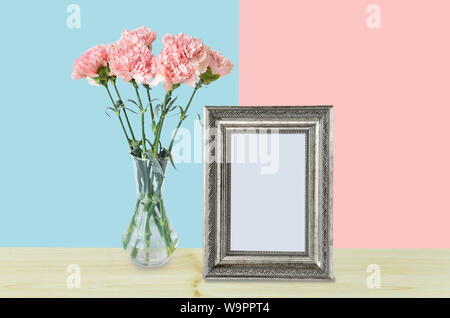 Home decor con un vuoto di argento photo frame e un mazzo di garofani rosa in un elegante vaso di vetro in rosa e gli sfondi blu Foto Stock