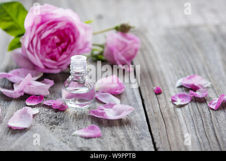 Flaconcino di vetro con rose olio essenziale e fiore di rosa rosa su uno sfondo di legno Foto Stock