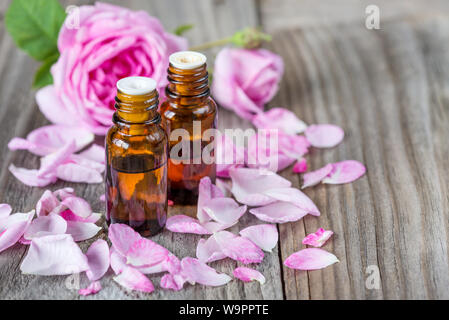 Due fiale di scuro con rose olio essenziale e le rose rosa su uno sfondo di legno con copy-spazio Foto Stock