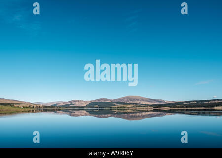 Clatteringshaws Loch nella foresta di Galloway in Scozia con il blu del cielo e le colline perfettamente riflessa nello specchio superficie calma del Loch Foto Stock