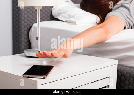 Donna di canto close-up cercando di raggiungere lo squillo del telefono cellulare o di allarme che hanno qualche funzione snooze di mattina presto. Foto Stock