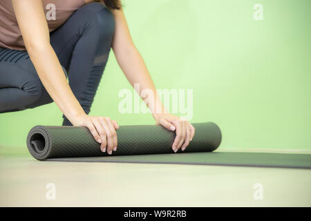 Giovane donna asiatica si concentra sul nero di rotolamento materassino yoga dopo yoga classe close up shot. Foto Stock