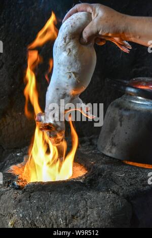 Donna locale azienda Cuy, giant cavia su fiamma aperta per rimuovere i capelli, la preparazione per la preparazione al tradizionale piatto Cuy, Cusco, Perù Foto Stock