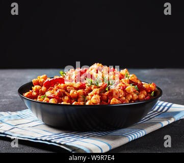 Garbanzos fritos, caldo stufato di ceci con affettato chorizo, prosciutto, pomodori e le spezie in una ciotola nero su un tavolo in cemento con sfondo nero dietro Foto Stock