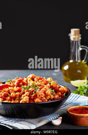 Garbanzos fritos, caldo stufato di ceci con affettato chorizo, prosciutto, pomodori e le spezie in una ciotola nero su un tavolo in cemento con ingredienti al black ba Foto Stock