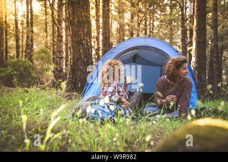Coppia di giovani donne alla moda di bere il tè e il caffè seduti in una tenda da campeggio alla moda ragazze sportivo rilassante nella foresta dopo una vacanza escursionistica Tour Foto Stock