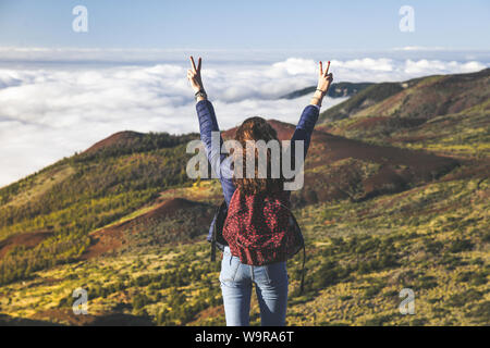 Adolescente con zaino e le mani alzate in piedi sulla cima della montagna con splendida vista a mare della foresta e le nuvole. Vulcano Teide Tenerife, Spagna. Annuncio Foto Stock