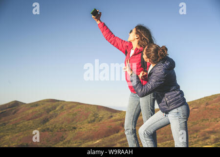 Coppia felice di adolescente in piedi su una montagna cliff edge, tenendo selfie con la new tech smartphone. Generazione z facendo le persone social video on-line. Annuncio Foto Stock