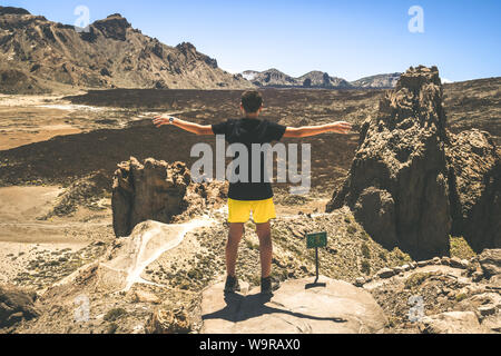 Ragazzo adolescente godendo all'aperto in piedi su una scogliera di montagna su Tenerife Teide National Park. Spensierato giovane maschio bracci sollevati godendosi il panorama Foto Stock