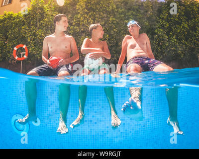 Tre giovani ragazzi divertirsi presso la piscina seduta con le gambe in acqua. Squalo Visualizza un gruppo di adolescente sorridente. Le persone che si godono la vacanza estiva Foto Stock