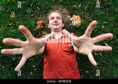 Un uomo stolto in una maglietta rossa si trova a terra tra i funghi Foto Stock