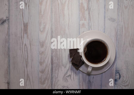 Nero caffè in una tazza bianca con un piattino e pezzi di cioccolato sulla parte superiore della tavola visualizza, sfondo per il testo Foto Stock