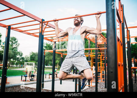 atleta forte che fa tirare-in su sulla barra orizzontale. Uomo muscolare che fa tirare su barra orizzontale in parco. Palestra Bar durante l'allenamento. Allenamento Foto Stock