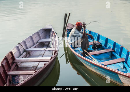 Il vecchio uomo seduto in una barca di legno di pesca mentre si fuma una sigaretta Foto Stock