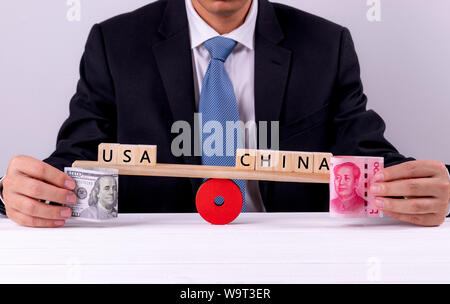 Closeup imprenditore il mano che tiene la banconota tra Stati Uniti e Cina sull'altalena. Guerra commerciale, Tariffa, barriera fiscale tra Stati Uniti e Cina concetto. Foto Stock