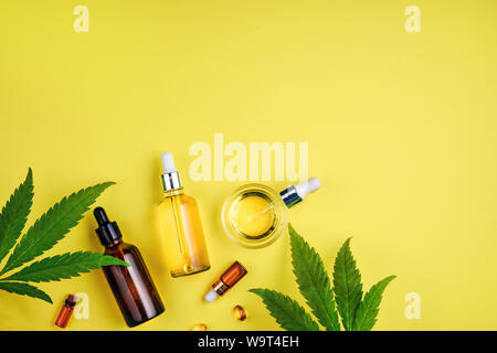 Bottiglie con olio di CBD, un contagocce e foglie di cannabis su uno sfondo giallo. Il concetto di cura di bellezza con olio di canapa Foto Stock