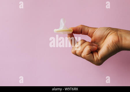 Femmina lato tenendo il preservativo sullo sfondo rosa Foto Stock